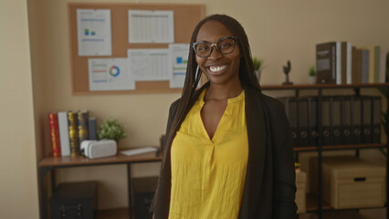 Woman smiling in an office setting shows confidence with curly hair and yellow shirt, surrounded by...