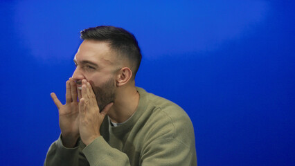 Energetic man shouting with cupped hands against vibrant blue background conveying excitement and...