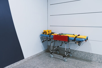 Empty hospital corridor corner with wheeled ambulance stretcher and spine board, safety straps and head immobilizer, modern clinic interior, emergency care concept, copy space