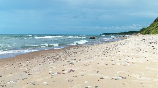 Sandy shoreline under bright blue sky, gentle waves rolling onto pebbled sand