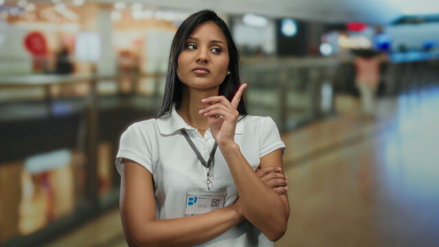 Woman contemplating in a busy mall, wearing a white polo with a thoughtful expression, capturing a scene of indoor shopping and thoughtful reflection.