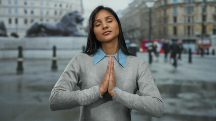Woman meditating with closed eyes on a city street, embracing tranquility among urban chaos with hands raised in a peaceful gesture.