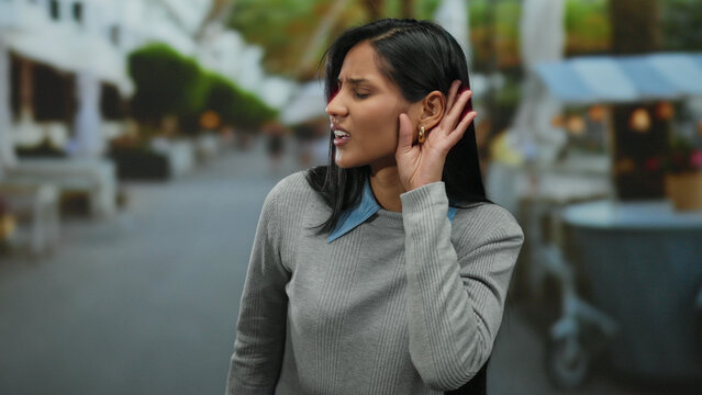 Woman on street listening gesture curious outdoor latin hispanic young daytime urban casual outfit neighborhood trees