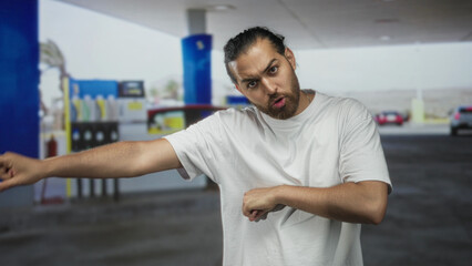 Man pointing with outstretched arm and arms crossed by gas pump on street forecourt canopy  anger confrontation tension. © Krakenimages.com