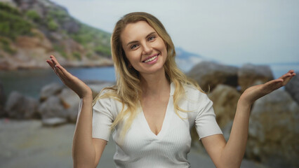 Young woman smiling at the seaside with blonde hair and a white shirt, enjoying the sunny outdoor...