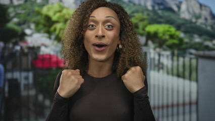 Woman clutching chest outdoors by iron fence and building in urban color street scene; astonishment.