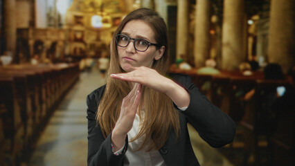 Woman standing in a church building holds hands in timeout gesture with closed eyes and furrowed brow; impatience.