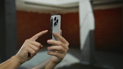 Man holding smartphone indoors at construction site with focus on hands as he navigates phone interface, suggesting modern technology usage in an unfinished home setting.