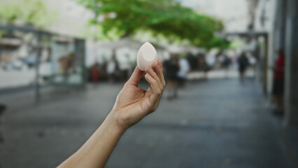 Hand of a caucasian man holding an egg-shaped object on a busy outdoor city street in daylight.