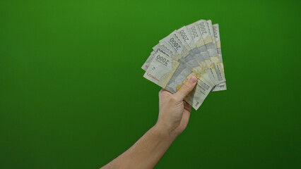 Caucasian man holds indonesian rupiah banknotes against a green background in a close-up shot...