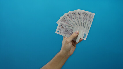 Man holding singapore dollars in a hand against a blue background, isolated and showcasing currency...