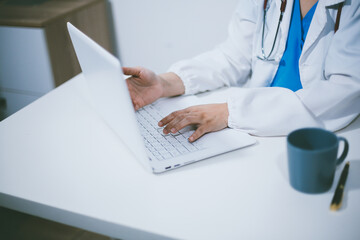 Fototapeta premium Middle aged female doctor working on laptop in doctor's room