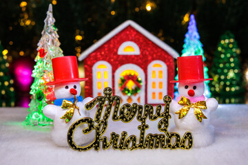 Snowmen in red hats with letters and a red house on a blurred Christmas background