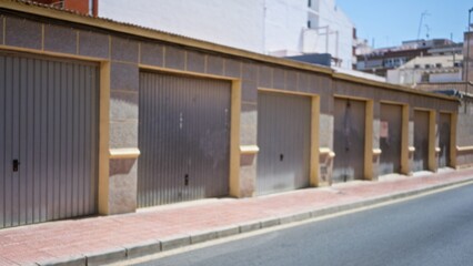 Obraz premium Row of metal garage doors along a sunlit sidewalk, defocused street background; backdrop template copyspace.