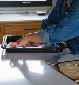 Mujer de piel morena pone papel manteca para hornaer galletitas sobre la mesada de la cocina
