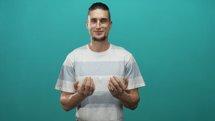 Man beckoning with hands toward camera on teal studio backdrop, wearing striped tshirt and slight smile; invitation calm.