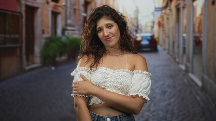 Naklejka premium Woman holds arm across chest showing shoulder and pearl necklace on cobblestone street; quiet contemplation.