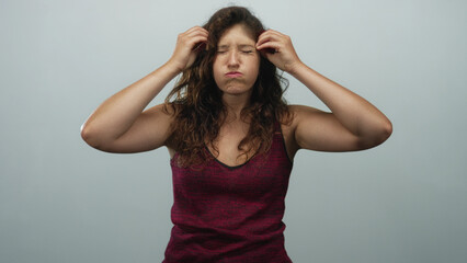 Naklejka premium Woman touching hair with hands raised and open mouth in light gray studio wearing maroon tank top; surprise reaction.