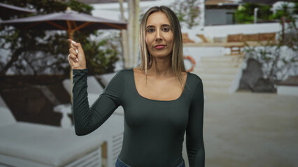 Obraz premium Woman finger pointing to umbrella in front of a building at an outdoor pool terrace; confidence leisure.