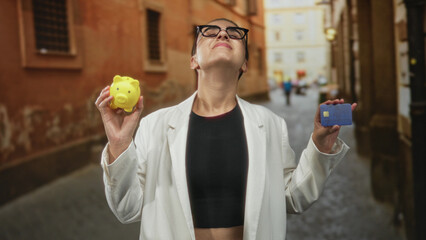 Woman holding a yellow piggy bank and a blue credit card while smiling and tilting her head on a...