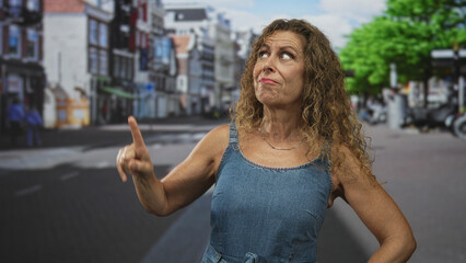 Fototapeta premium Middle aged woman with bare arms and hands on hips, smiling and looking up on a street; confidence resilience.