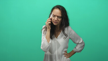 Woman holds smartphone to ear with arms crossed and tense expression in studio; frustration...