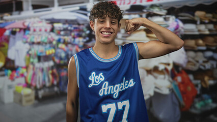 Teenage boy flexes biceps in street market wearing blue los angeles basketball jersey 77, smiling...