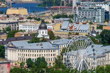 Rooftops of historical Podil district in Kyiv, Ukraine. Ferris wheel and rounder building of famous Kyiv-Mohyla Academy. Harbor on Dnieper river on background