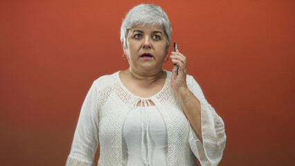 Woman in white blouse holding smartphone to ear, talking and reacting with open mouth and raised...