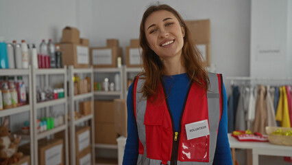 Volunteer woman smiling indoors at a charity center filled with donation supplies and organized storage shelves highlighting community spirit and humanitarian efforts.