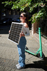 Woman using portable solar panel to charge scooter, highlighting integration of sustainable renewable energy. Green electric scooter connected to solar panel, emphasizing eco-friendly transportation.