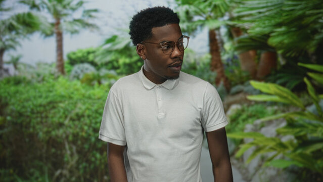 Man adjusts glasses on his face along a leafy forest path in warm morning sunlight; quiet reflection. - Powered by Adobe