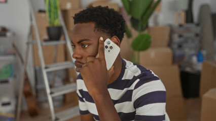 Man holding white smartphone points finger to temple in a modern home building interior with stacked moving boxes and a ladder; thinking.