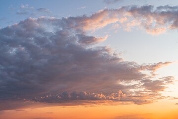 Sunset scene with orange, pink, yellow hues warm glow illuminating light gray clouds contrasted by darker gray ones hill or mountain silhouette in the distance horizon marked by a faint line