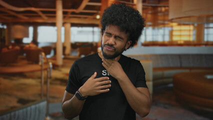 Man coughing and feeling unwell, wearing staff uniform in an indoor restaurant setting, conveying a...