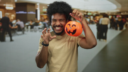 Man holding pumpkin basket in busy airport indoor scene, expressing playful excitement, surrounded...