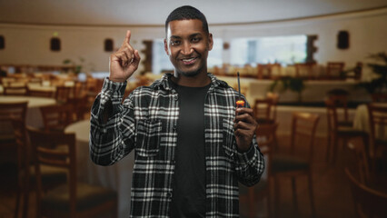 Man holding screwdriver points index finger up in a restaurant building while smiling and looking upward; confidence guidance.