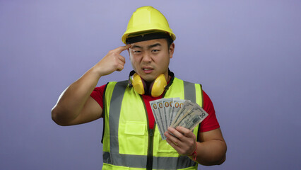 Young man wearing helmet holding us dollars with a thoughtful expression against a purple background.