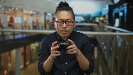 Man holding a game controller with both hands in a shopping building, eyes narrowed while playing a handheld game; focused concentration.