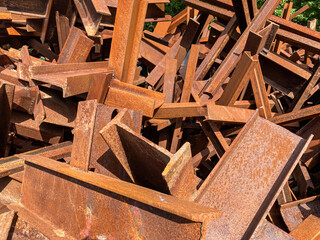 A pile of weathered, dark brown metal beams with rust patches, arranged haphazardly A white rectangular object, possibly a sign or panel, stands out among them Sunlight filters from the upper right
