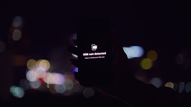 Smartphone Displaying SIM Not Detected Warning Held Against Night City Bokeh in a Close Angle Dark View Showing SIM Failure Situation