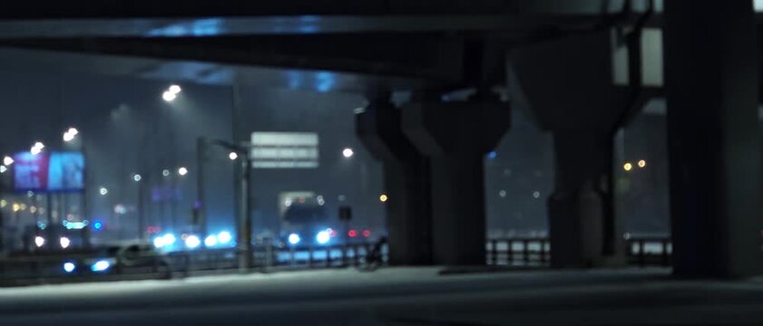 Night city traffic under elevated highway interchange with concrete columns street lights and blurred car lights creating cinematic urban infrastructure atmosphere