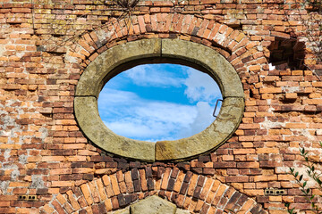 Blue sky with clouds through oval stone historic window in old abandoned brick wall, symbolising opportunity, future, openness and connection between past and new possibilities. Concept of memory
