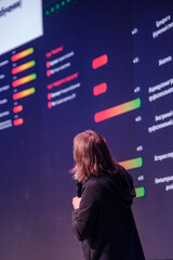 Bright data visuals illuminate speaker facing giant display with colorful bars and charts.