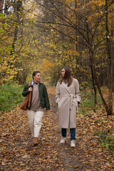 Fototapeta premium Two women walk together along a forest path covered with autumn leaves, tall trees around, natural daylight, relaxed and friendly atmosphere