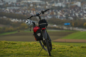 Bicycle with gear on hilltop overlooking city. Bicycle with bags and helmet parked on hilltop, with...