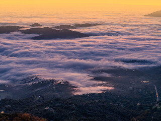 Sunset above thick foggy clouds layer rolling over distant mountains and dusk valleys, aerial view from above.