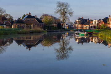 Perfect reflection of the Dutch town Bedum on the canal surface. Traditional brick houses, boats and spring trees in calm morning light