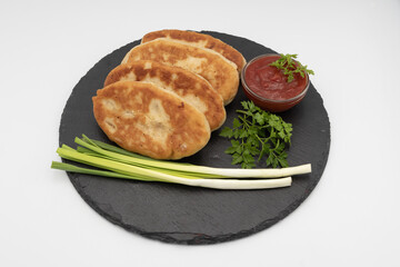 Homemade fried potato pies served with tomato sauce and fresh herbs on black slate plate