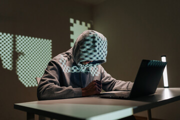 Mysterious person hoodie and glasses concentrating on laptop, depicting themes of cybercrime, hacking, data security, digital fraud and internet privacy issues in dark room.
